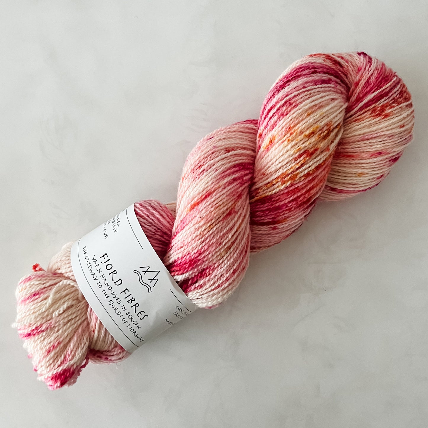 Hand dyed pink and white yarn with a Fjord Fibres label on a light background