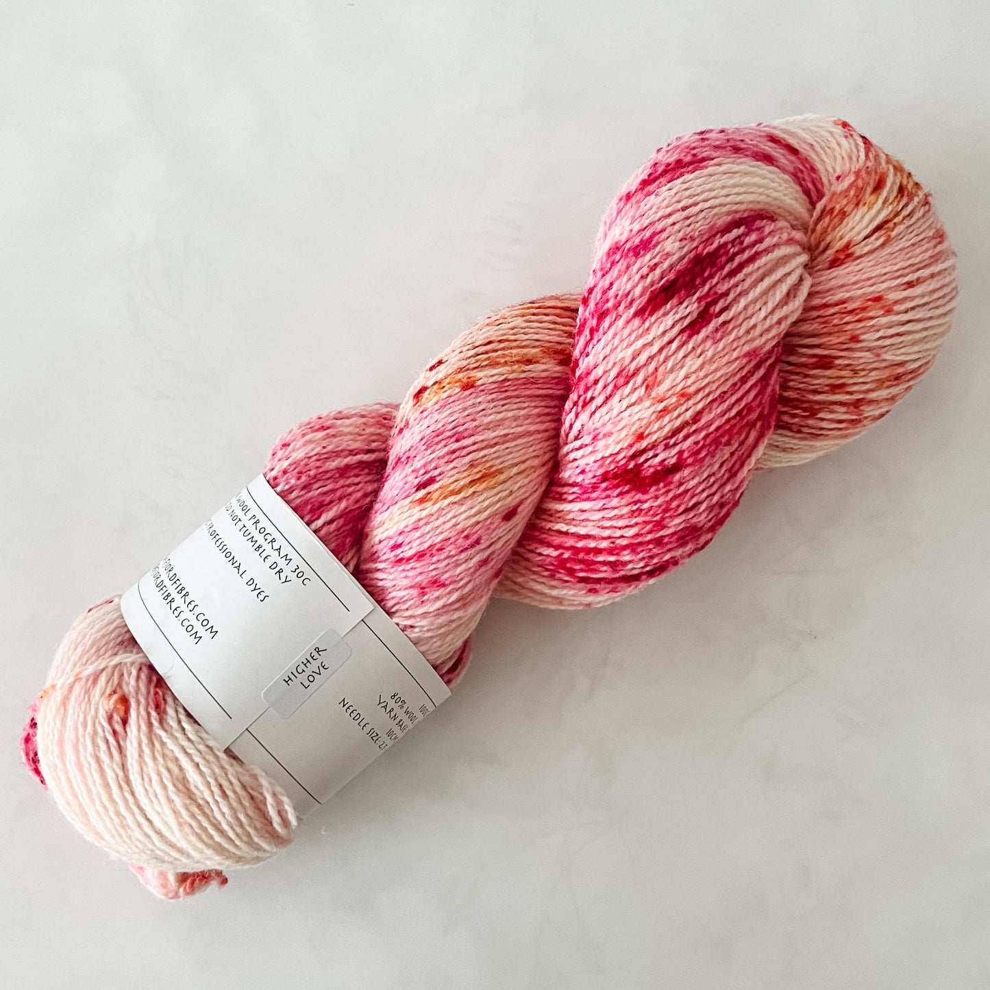 Hand dyed skein of pink and red Fjord Fibres yarn on a white surface